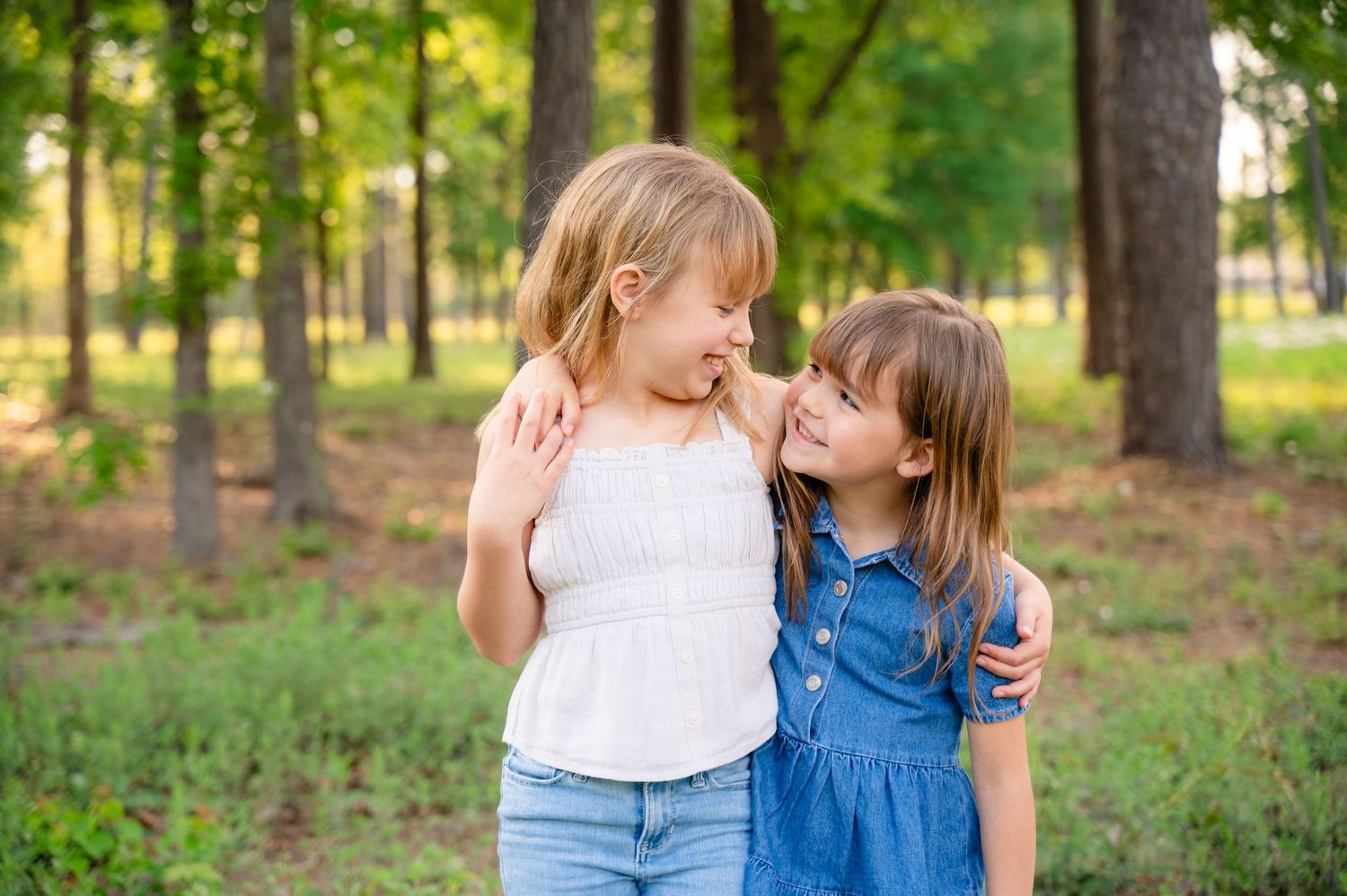 Two young children sharing a tender moment while embracing in a sunlit forest setting.