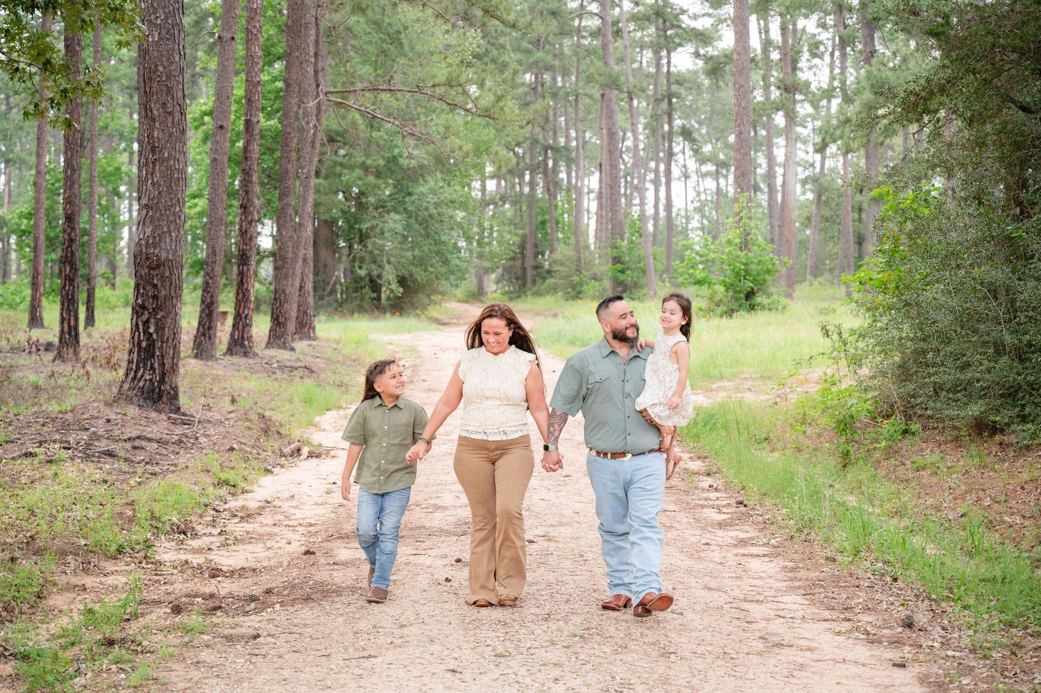 Family walking together on peaceful wooded trail surrounded by tall pine trees.