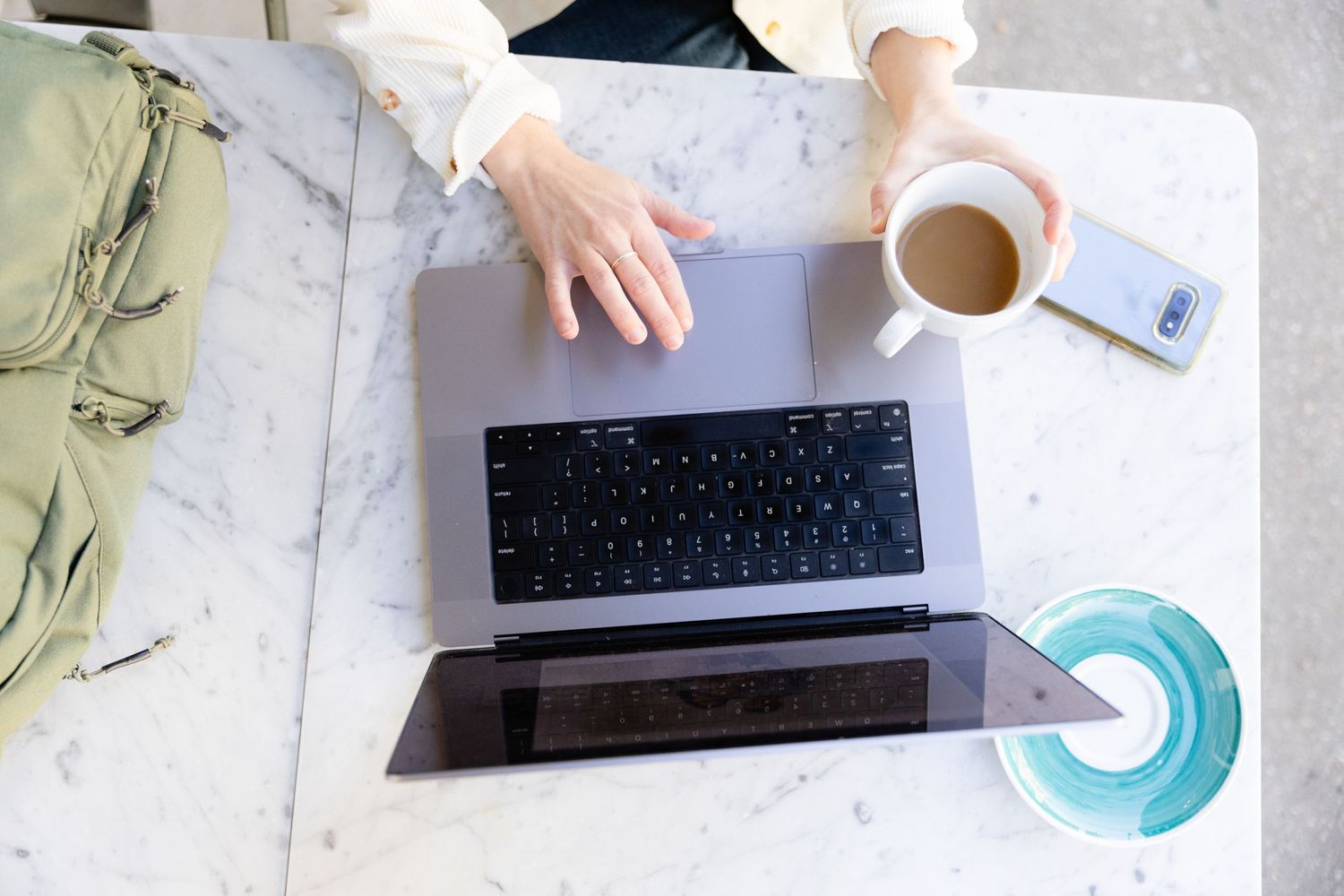 Overhead view of person working on laptop with coffee on marble surface.