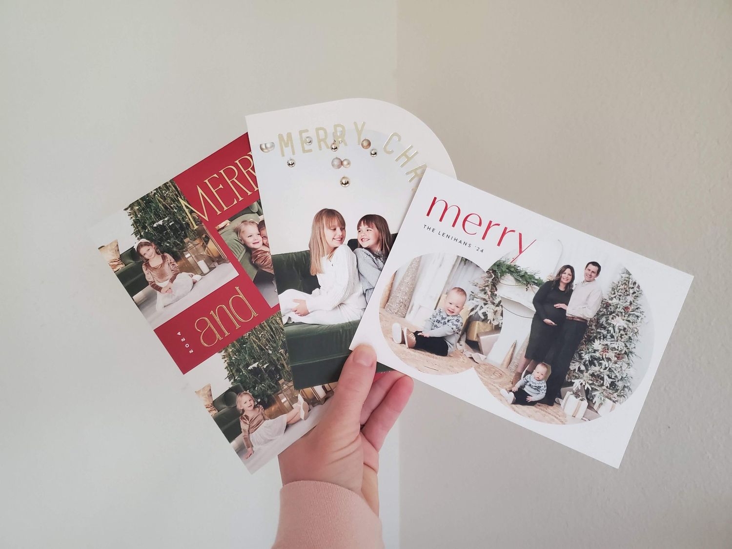 A hand holds multiple holiday photo greeting cards featuring festive designs and photographs.