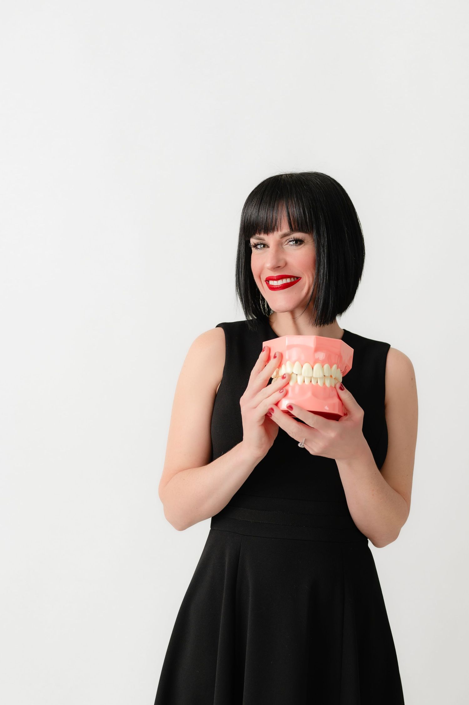 Woman in black dress holding dental model against white background.
