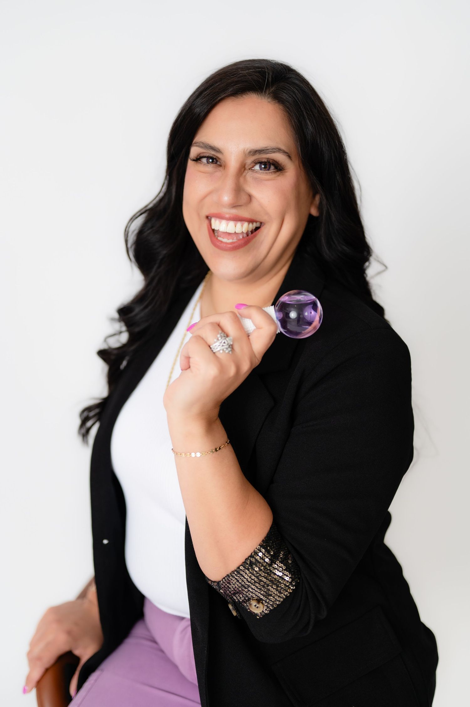 Professional portrait of someone wearing a black blazer and white top against white background with stylish accessories.