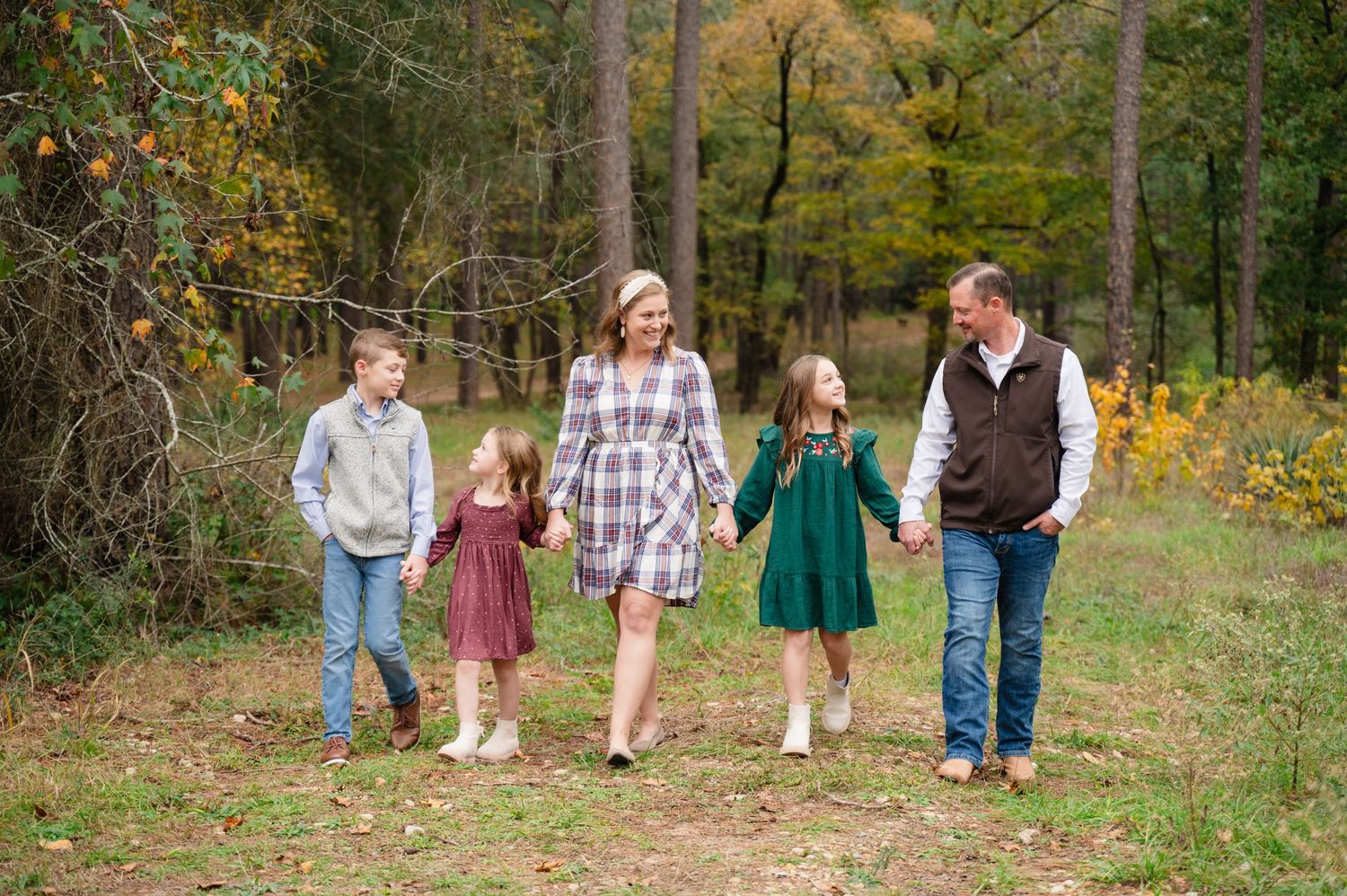 A family walks together holding hands on an autumn path surrounded by colorful fall foliage.