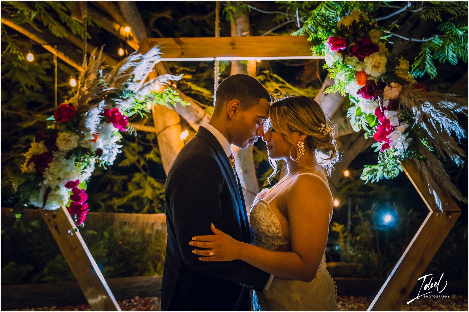 Couple sharing an intimate moment under a illuminated geometric arch with floral decorations.
