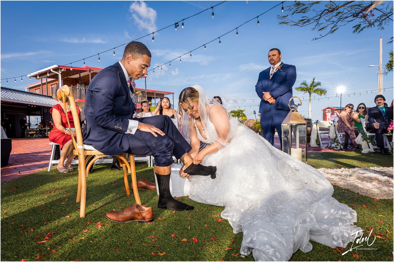 Outdoor wedding reception game played on lawn with string lights and red building in background.