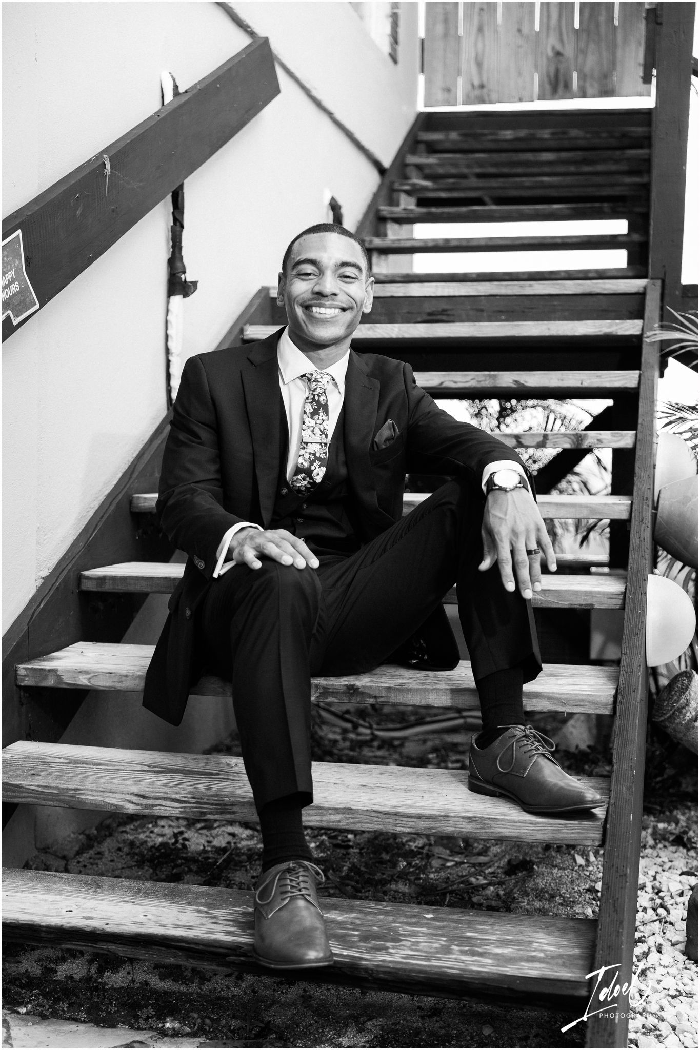 Black and white portrait of person in suit sitting on wooden stairs.