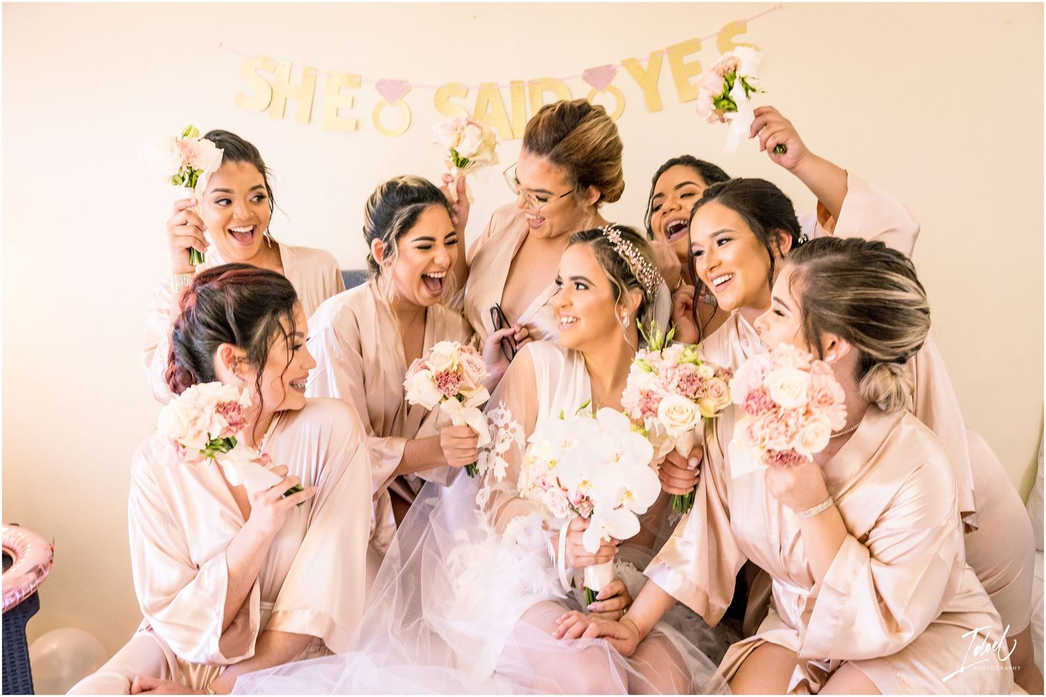Joyful bridal party in matching pink robes laughing together during pre-wedding preparations.