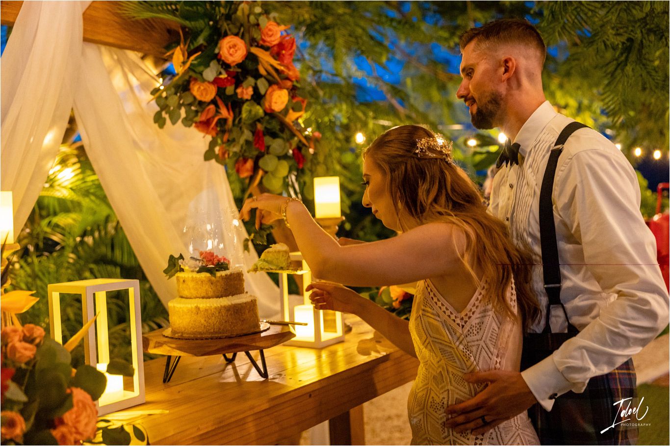 Couple cutting their wedding cake at rustic dessert table with lanterns and floral decorations.