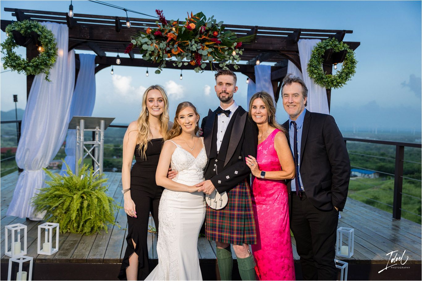 Wedding celebration group photo on an outdoor deck with mountain views and elegant decorations.