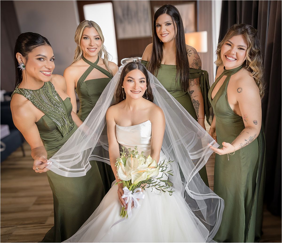 A bride in a white wedding gown stands with bridesmaids wearing sage green dresses during a wedding celebration.