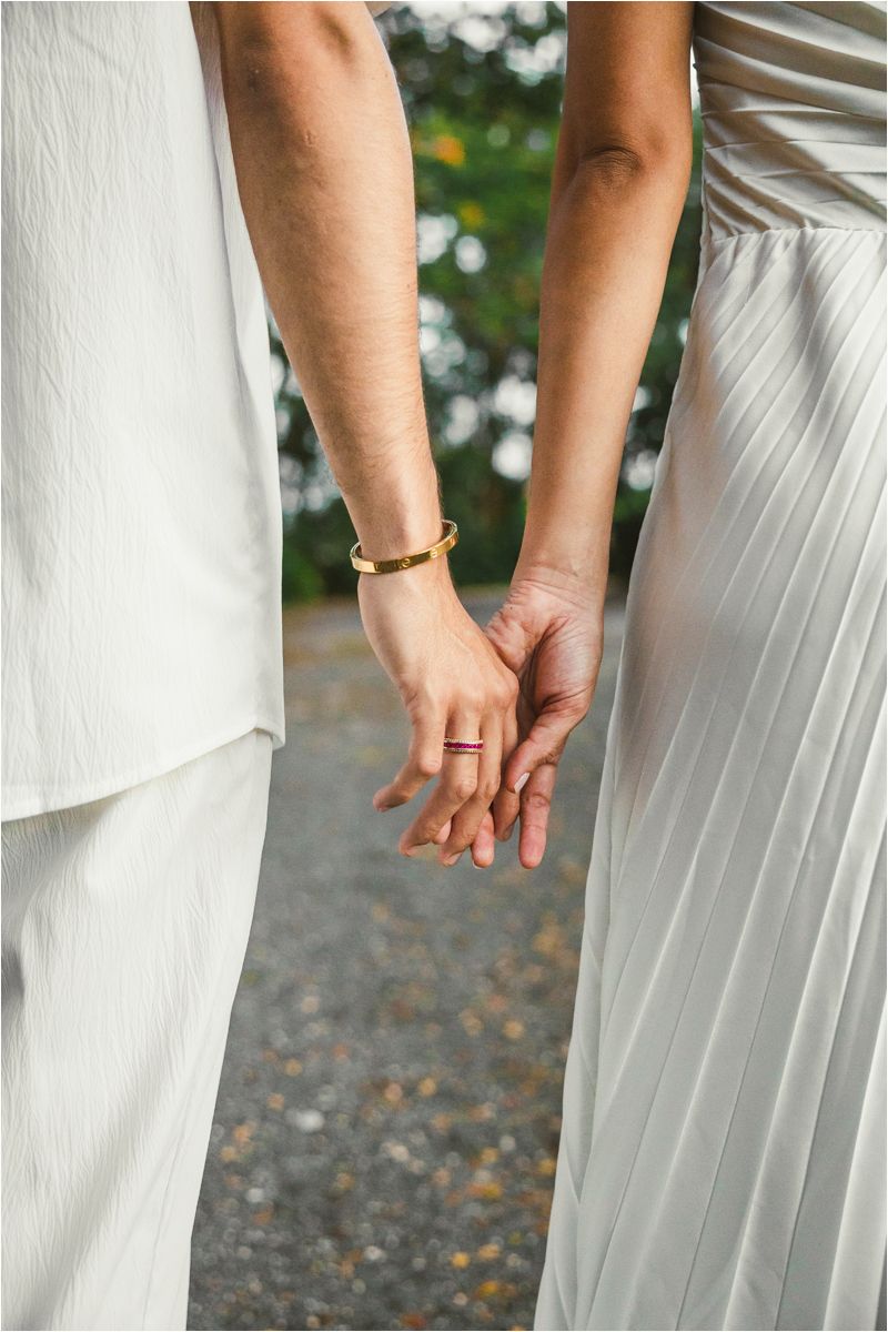 Close-up of couple holding hands wearing white wedding attire.