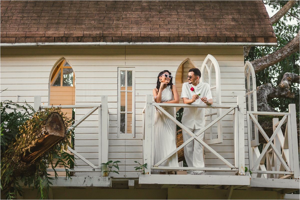 Wedding couple poses playfully on white porch balcony of rustic house in romantic outdoor setting.