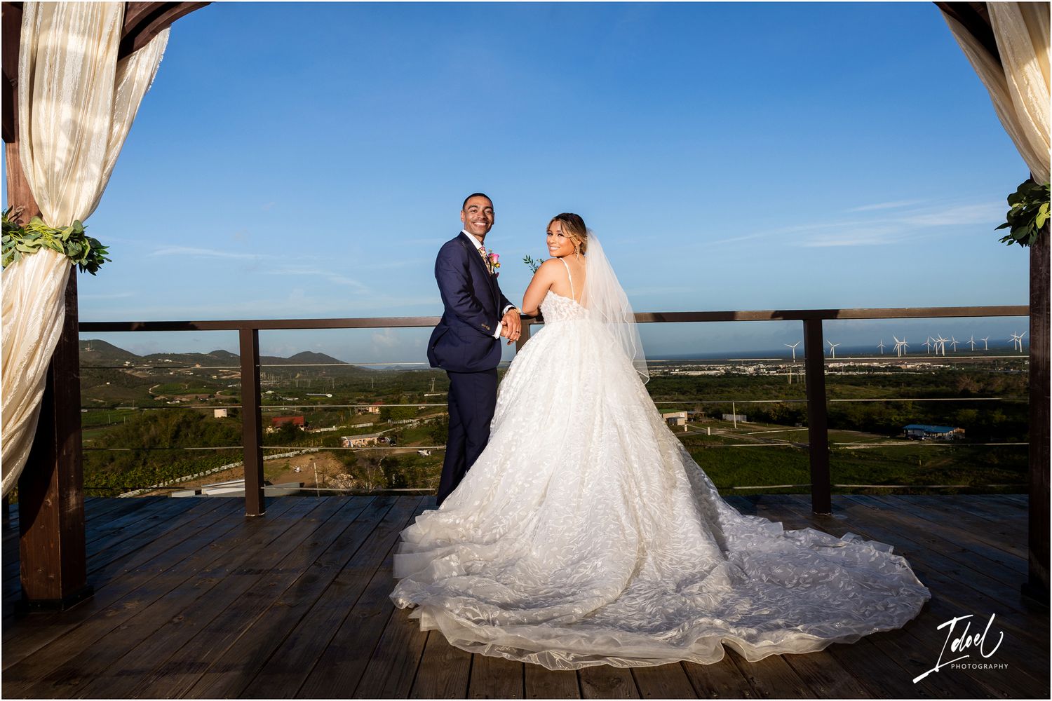 Wedding couple poses on scenic deck with dramatic ocean view and flowy veil.