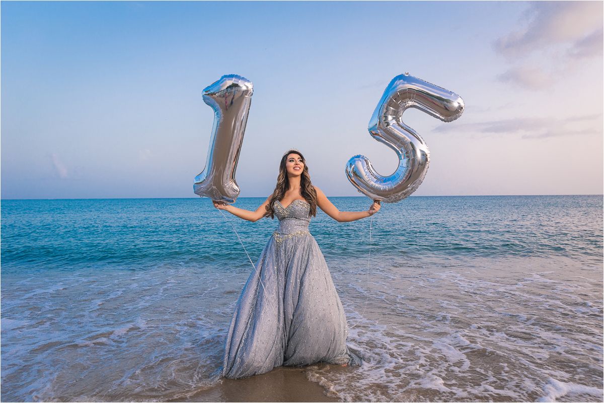 A flowing white dress billows in the ocean breeze as waves lap at the shoreline during a dreamy beach photoshoot.