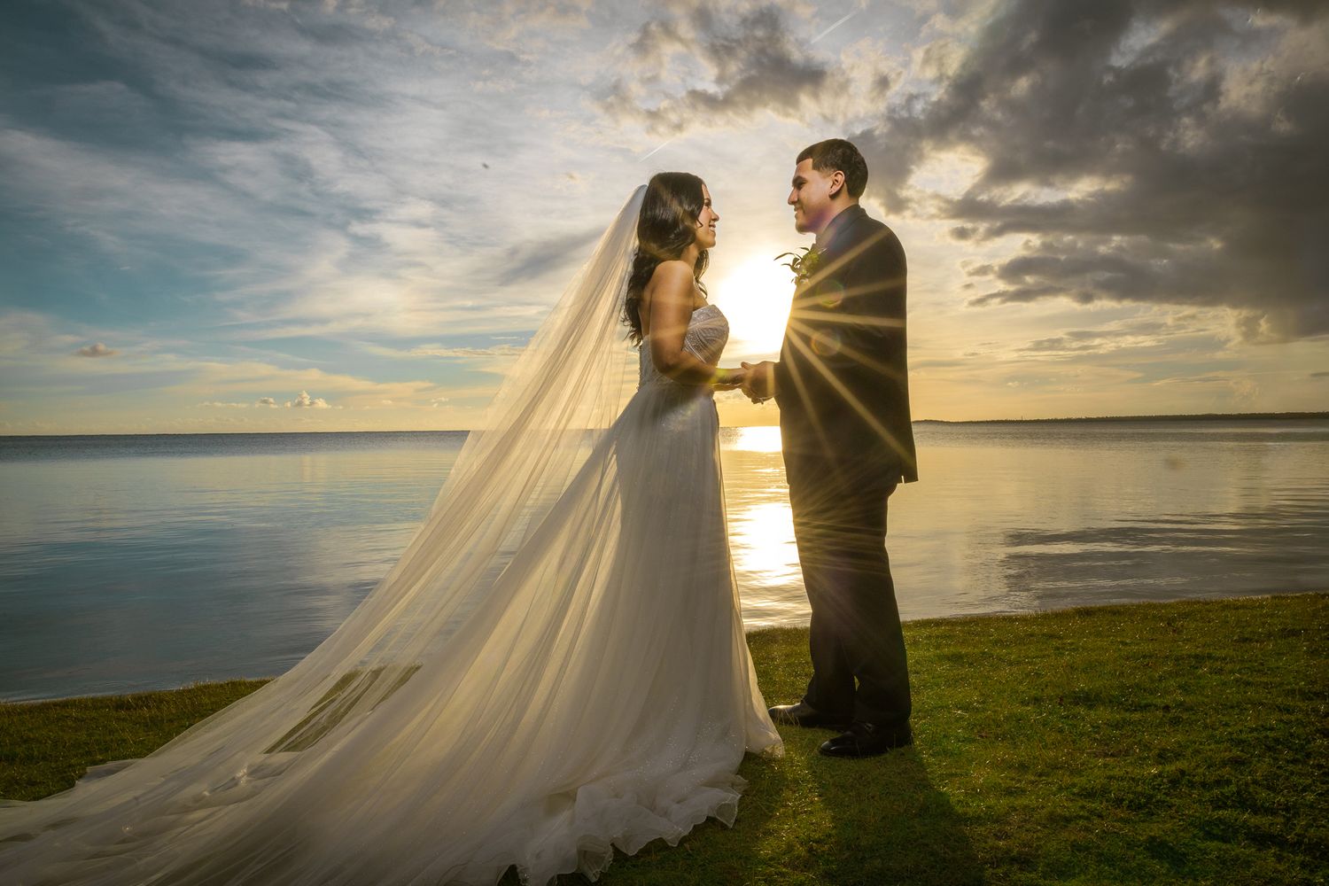 Sunset wedding portrait by the water with dramatic flowing veil.