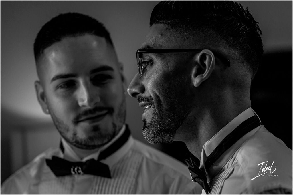 Black and white candid photo of two well-dressed men in bowties sharing a moment at a formal event.