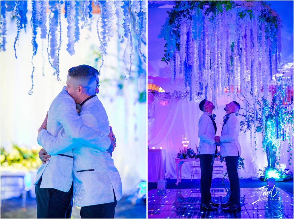 Two romantic silhouettes share a tender moment under blue and purple hanging flower decorations at an elegant wedding venue.