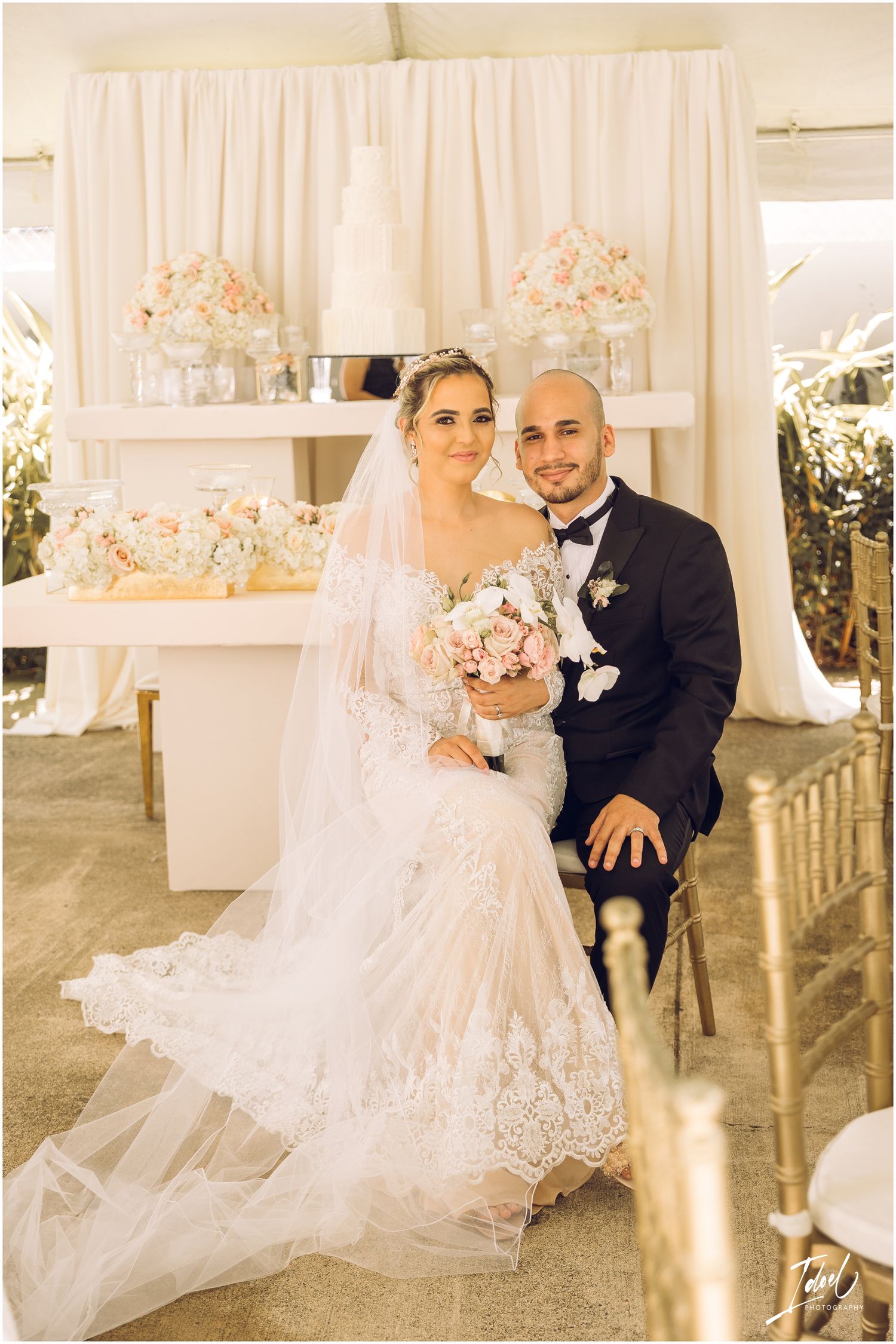 Elegant wedding portrait with cream backdrop, pink floral arrangements and detailed lace gown.
