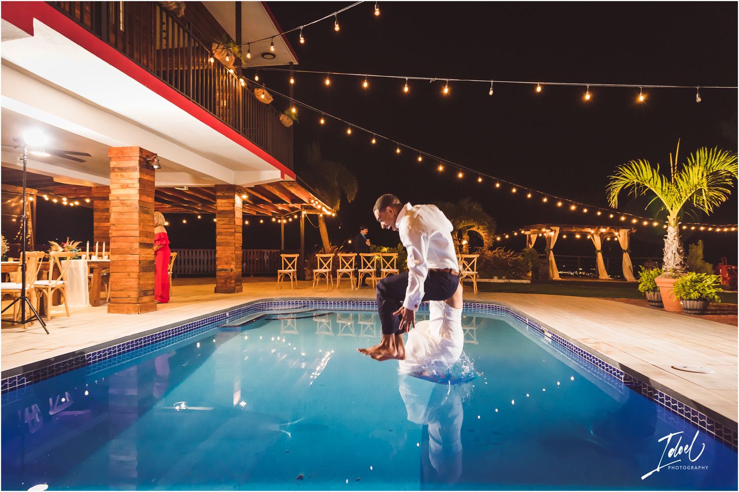 Wedding celebration splash into an illuminated pool with string lights overhead.