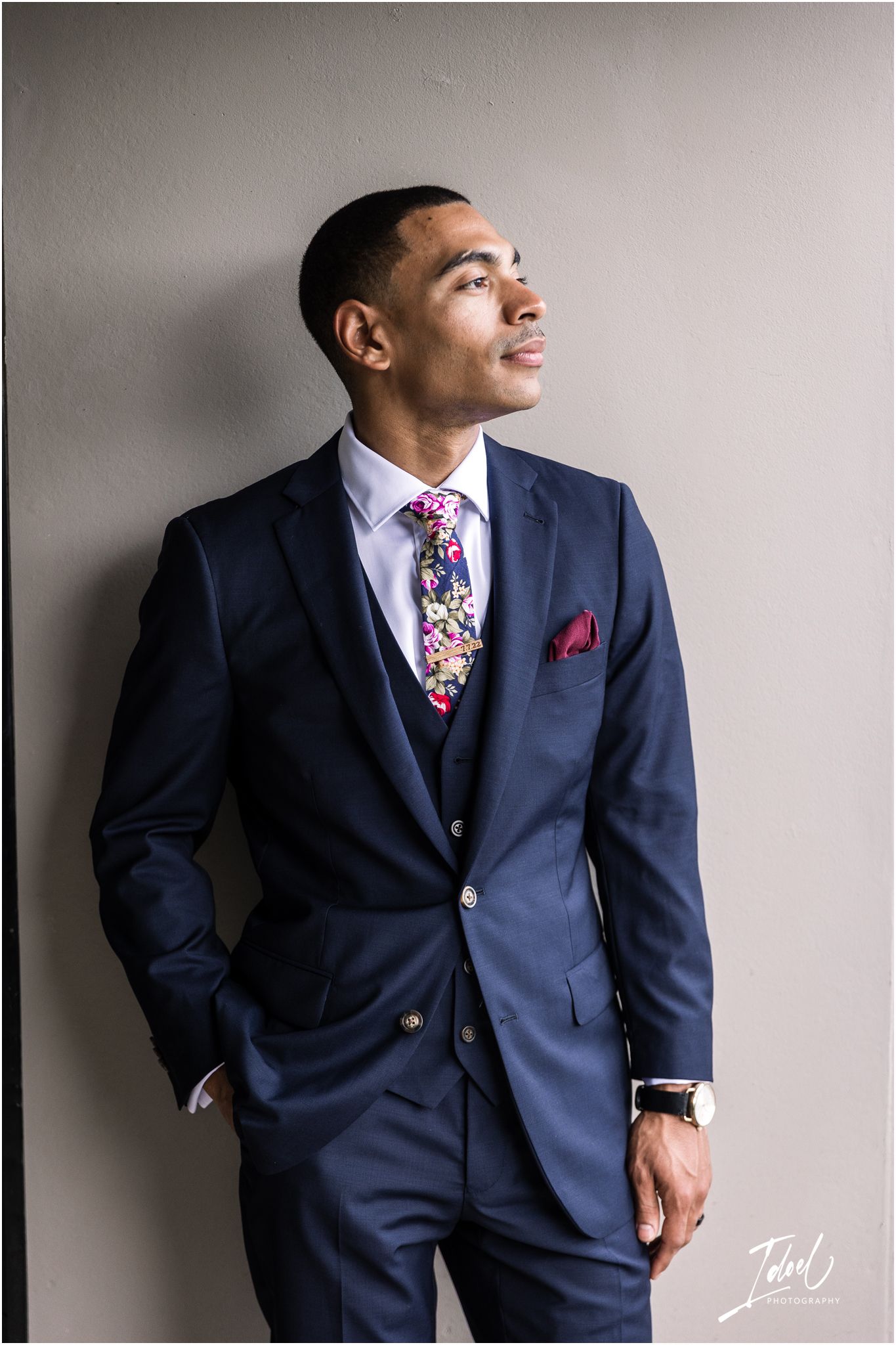 Professional portrait of person in navy suit with floral tie against neutral background.
