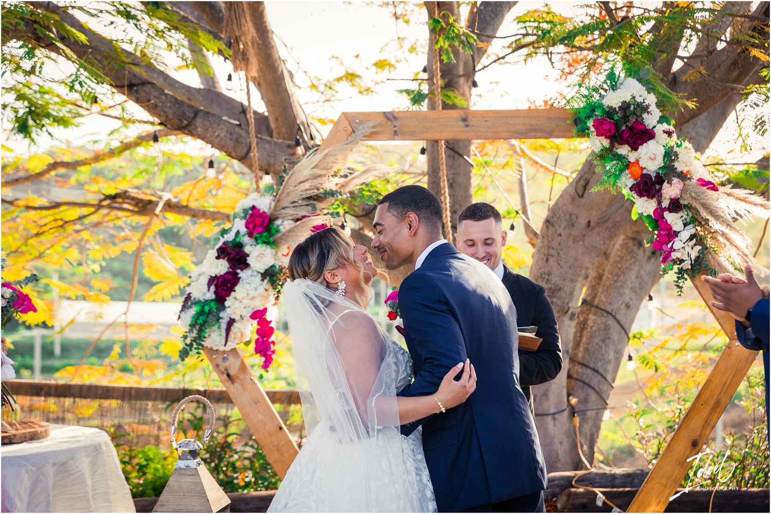 Beautiful outdoor garden wedding ceremony under flowering trees with pink floral arch.