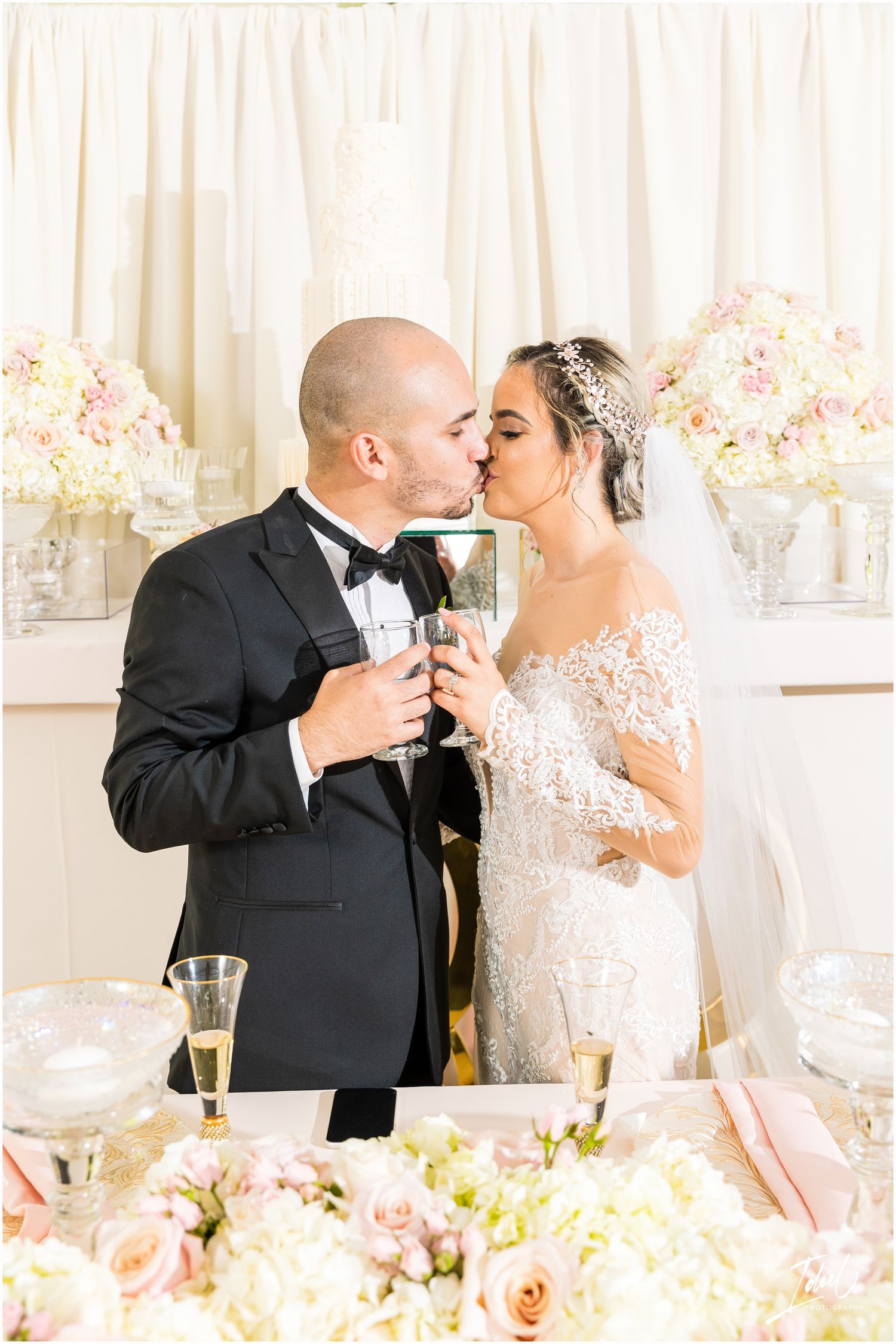 Newlyweds share an intimate champagne toast at their elegant wedding reception with pink floral decor.