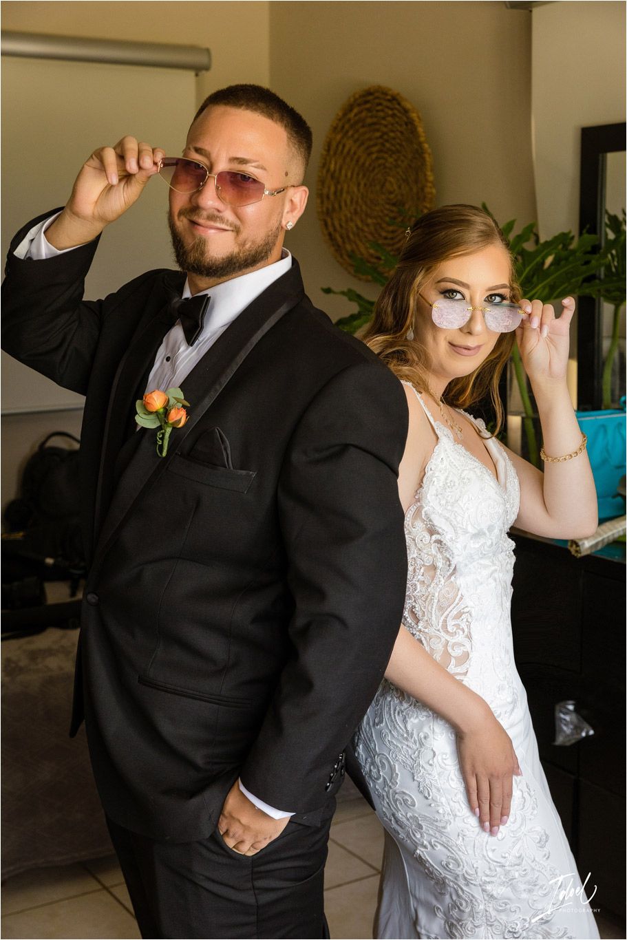 Wedding couple in formal attire striking a pose with sunglasses in an indoor setting.