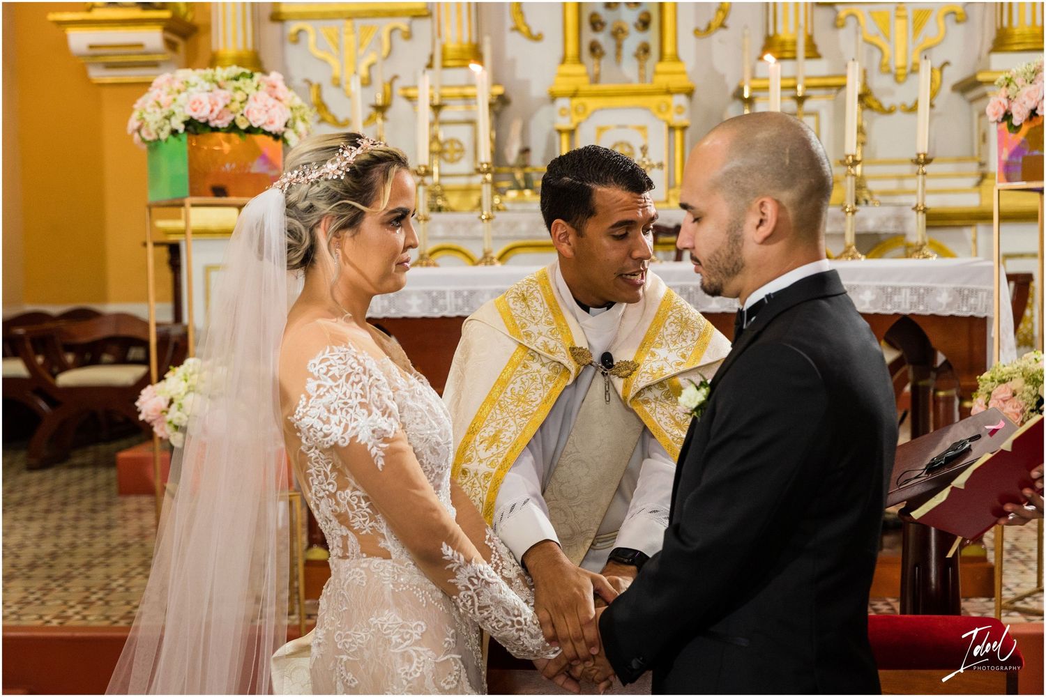 Catholic wedding ceremony with priest officiating in front of decorative church altar.