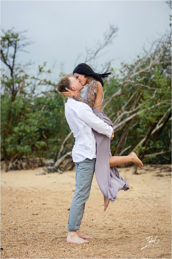 Joyful couple sharing a playful moment as one lifts the other on a beach path.