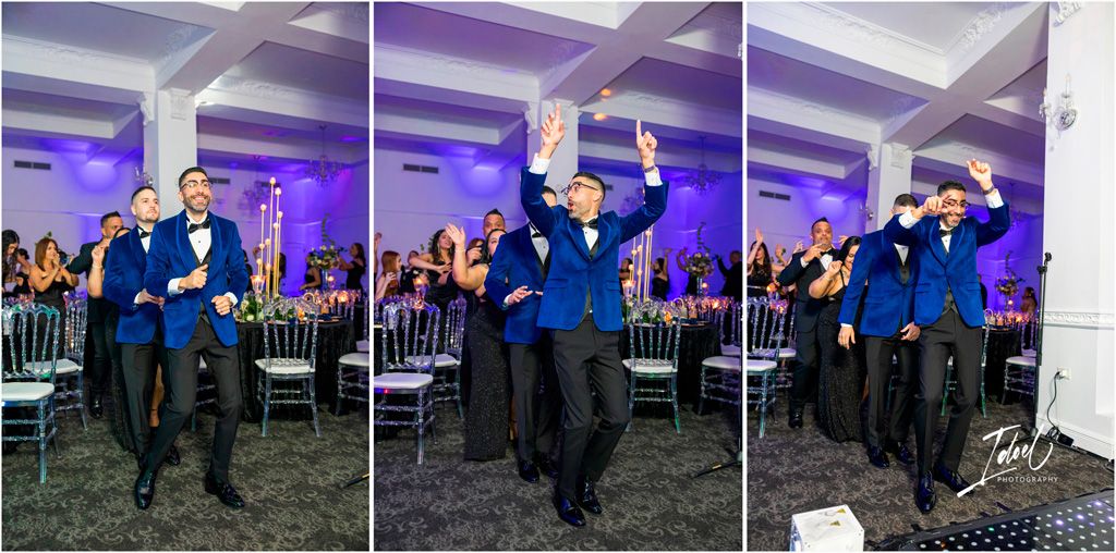 Three people in dark suits and blue vests dance energetically at a wedding reception with purple lighting.