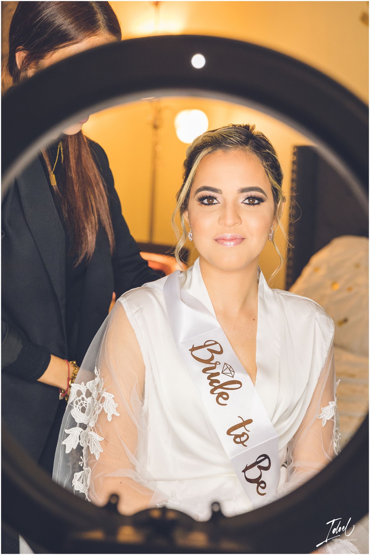 A ring light reflection shows wedding preparation scene in warm ambient lighting.