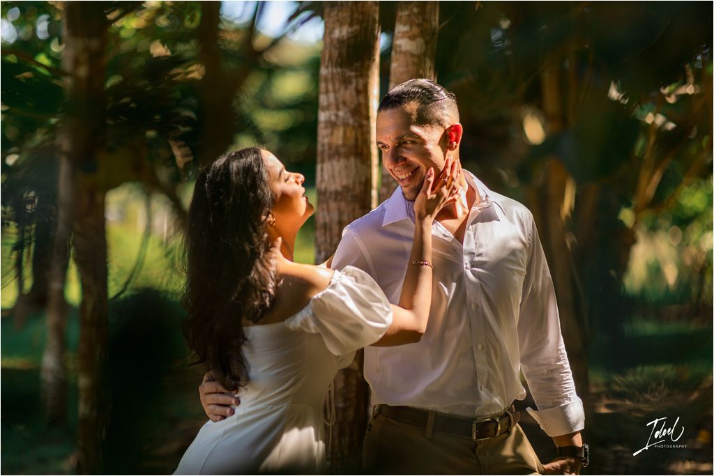 A romantic couple shares a tender moment in a sun-dappled forest setting during a golden hour photoshoot.