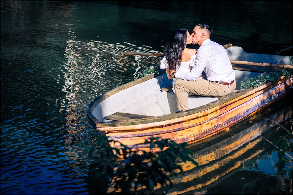 A couple shares a romantic moment in a rustic wooden rowboat on dark blue waters at dusk.