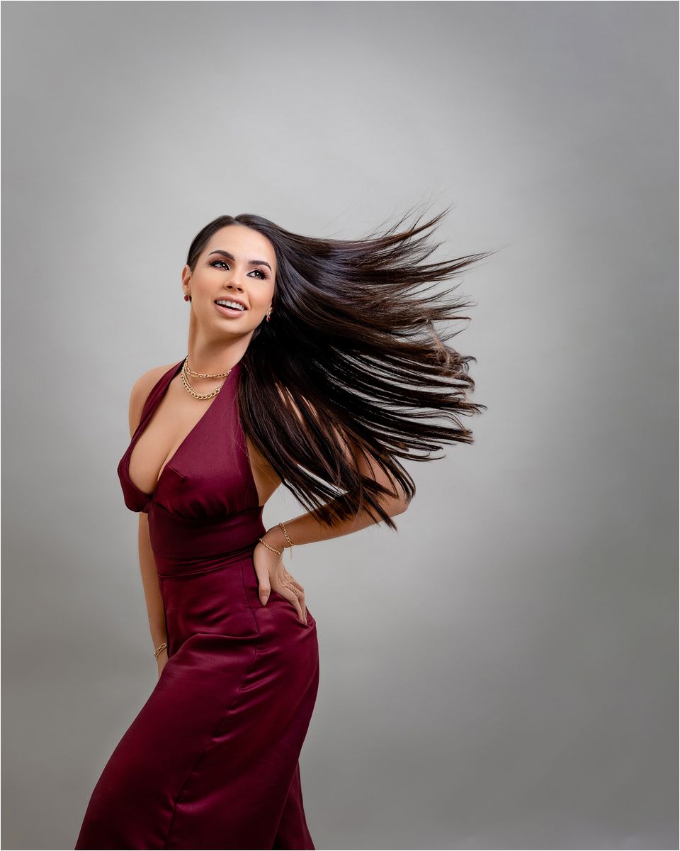 A dancer in a burgundy dress creates dynamic motion with flowing hair against a gray studio backdrop.