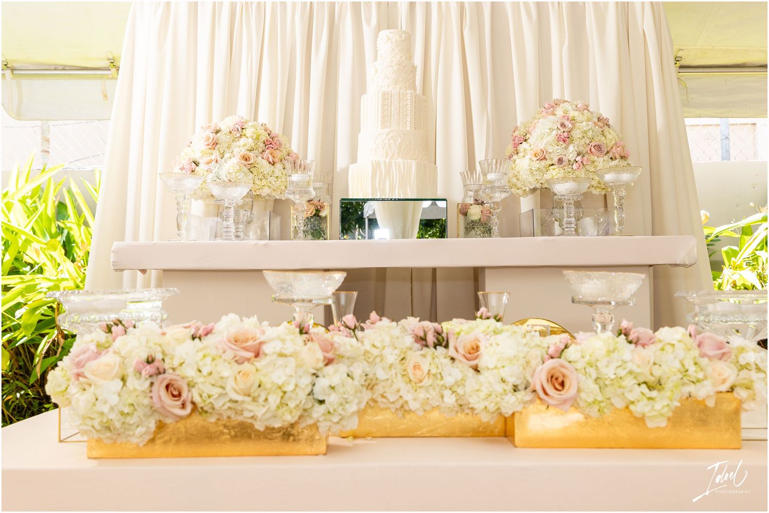 Pink and cream floral arrangements displayed on white shelving at a wedding reception.