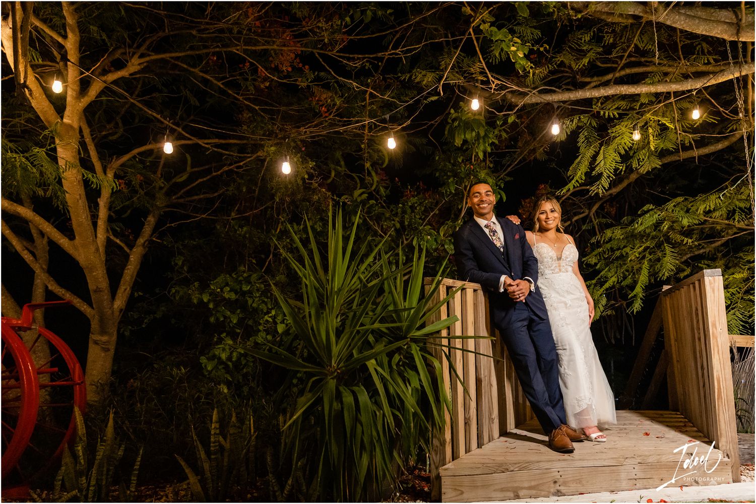 Romantic evening wedding scene on a wooden deck with string lights overhead.