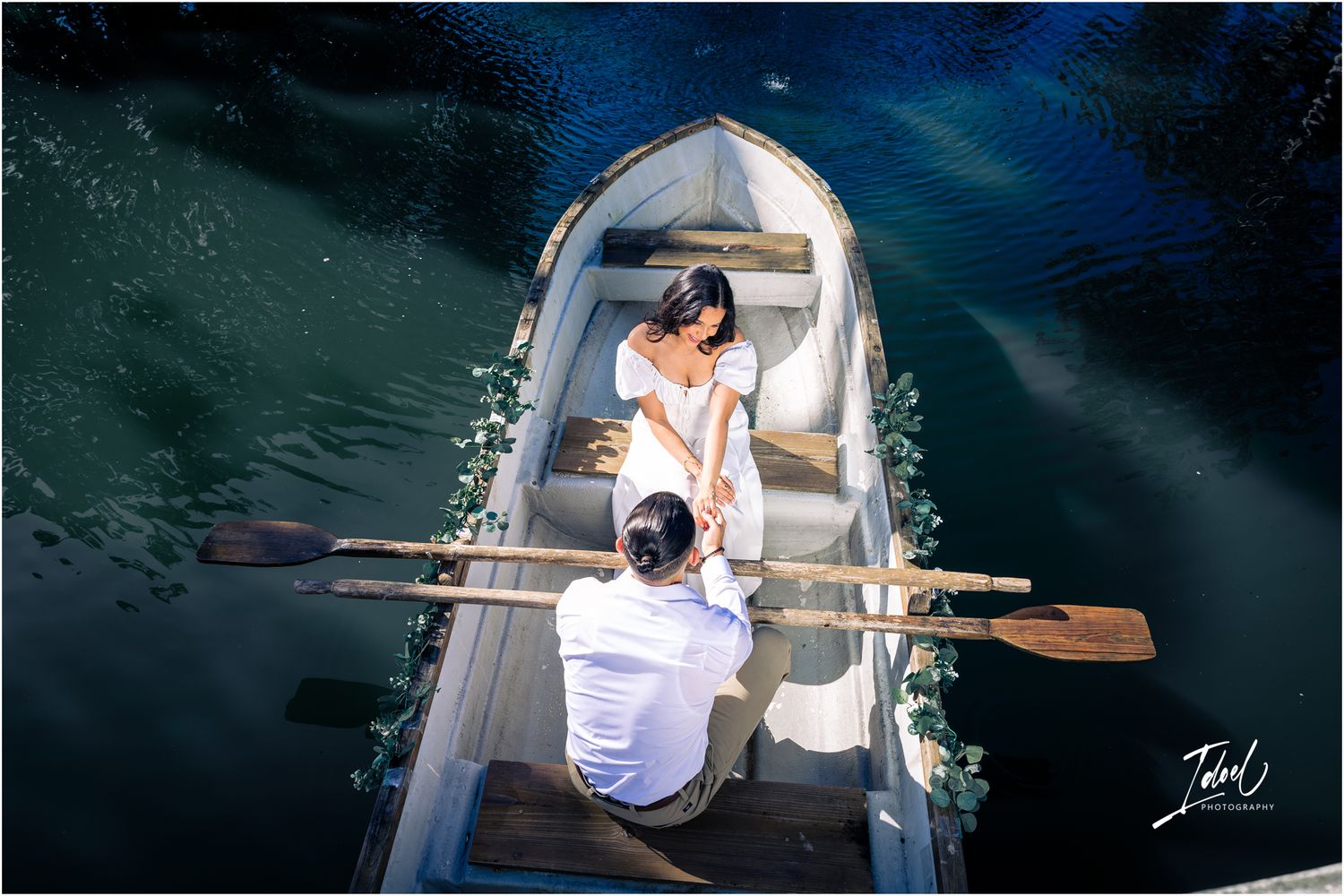 A couple in a small white rowboat on dark waters share an intimate pre-wedding photography session.