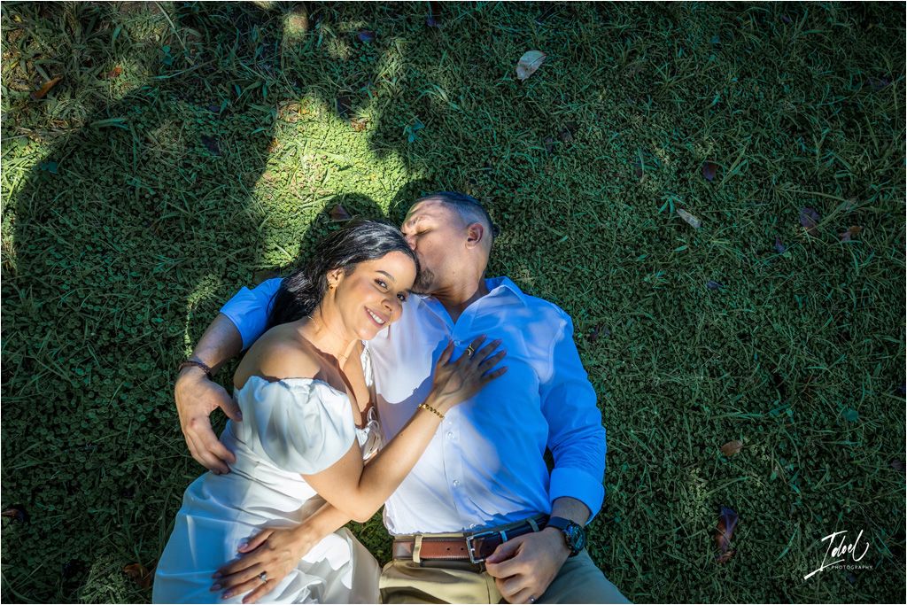 A couple lies together on green grass during a sunny outdoor photo session in romantic poses.