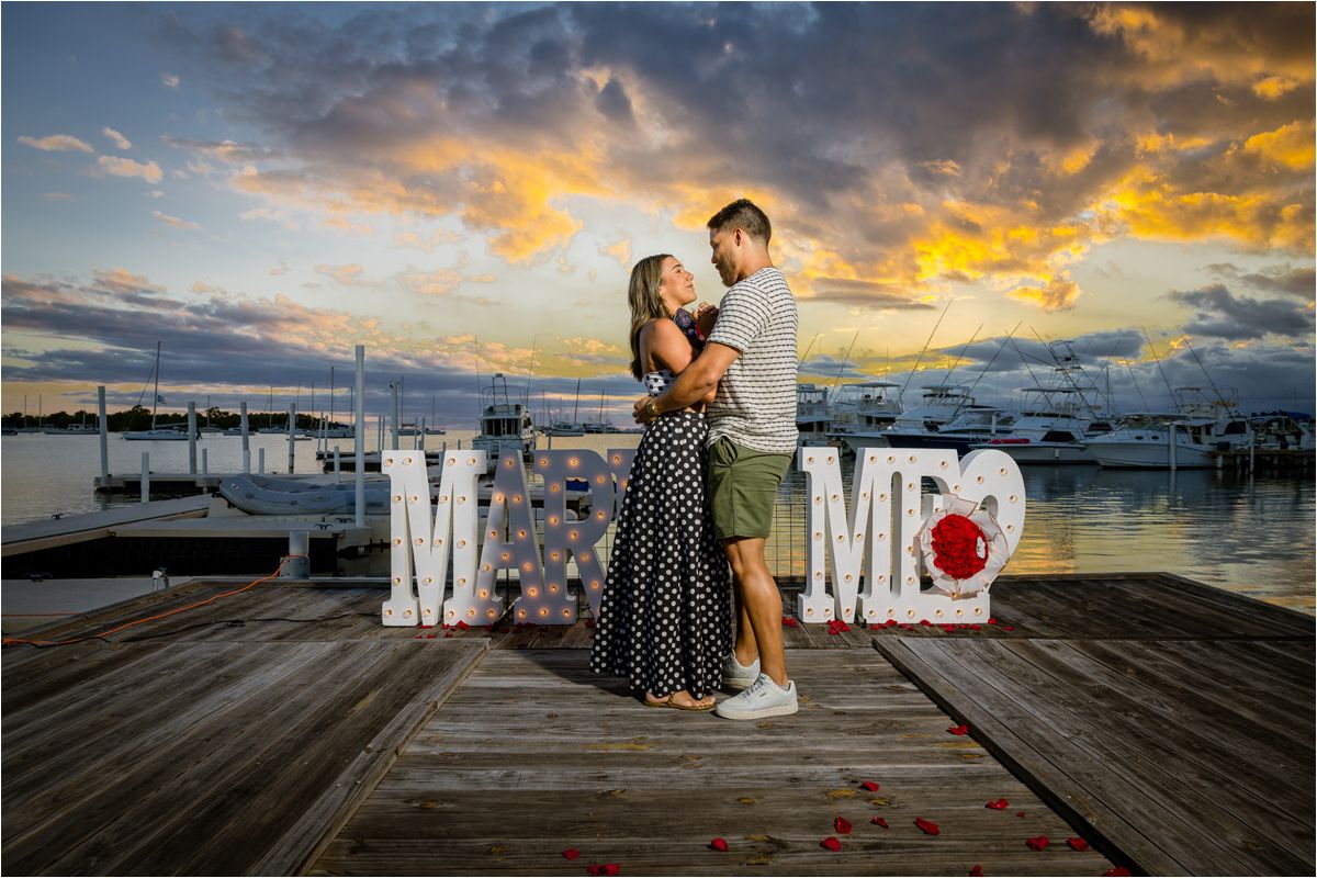 A romantic proposal scene on a dock at sunset with a 