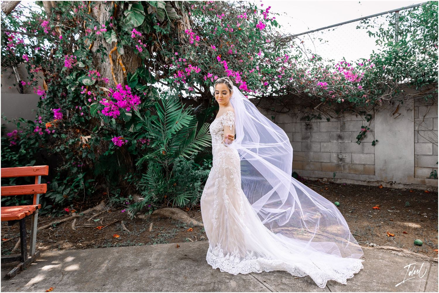 Flowing wedding dress and veil captured in garden setting with blooming bougainvillea.