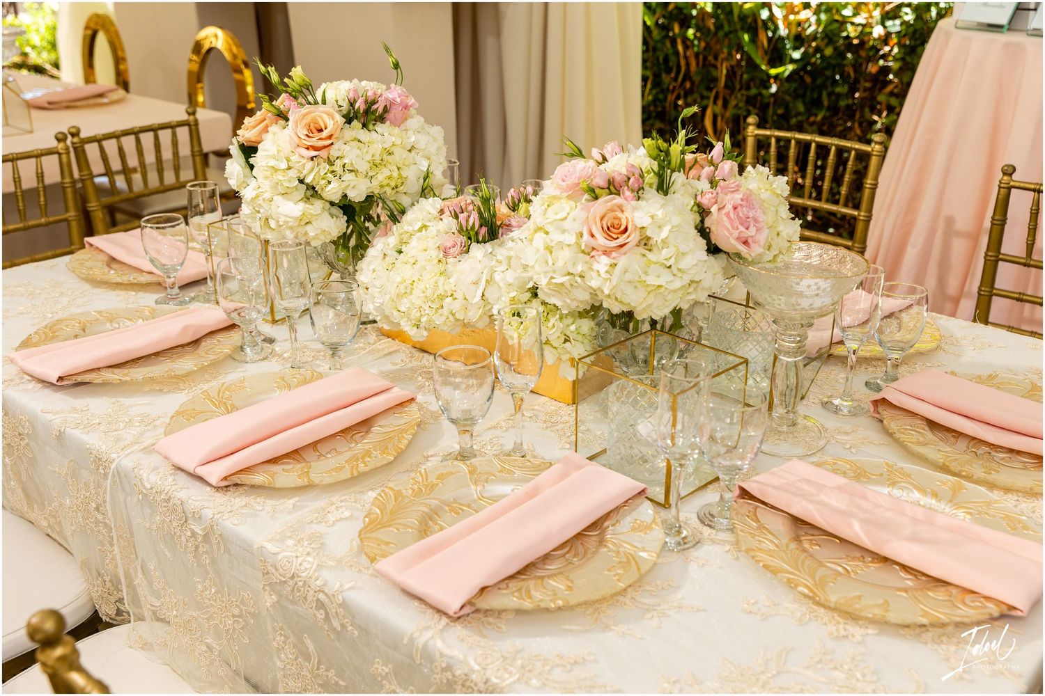 Wedding table settings with pink napkins, gold chargers and white floral centerpieces.