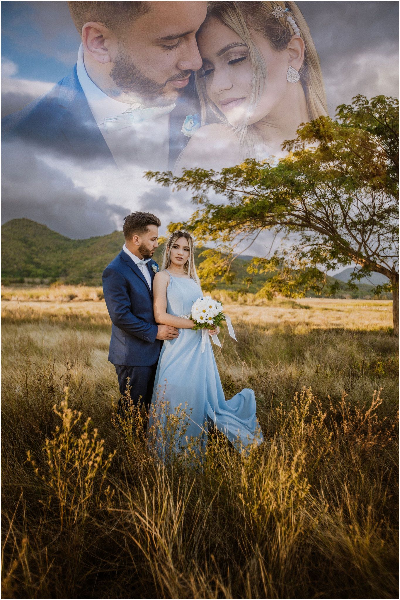 Romantic couple in formal wear standing in tall grass with mountains and dramatic sky behind them.