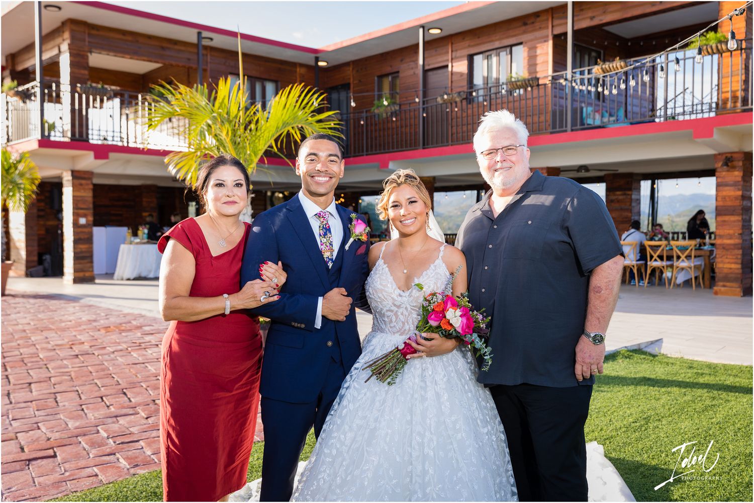 Wedding party portrait outside Spanish-style venue with red brick patio and balcony.