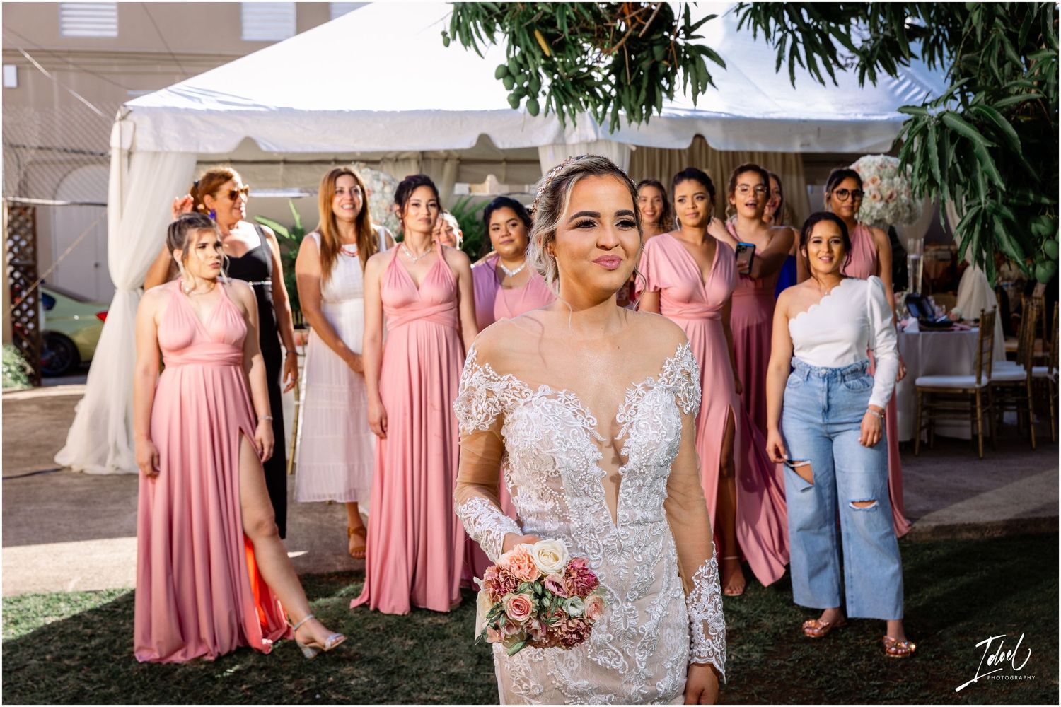 Wedding party gathered outdoors wearing pink bridesmaid dresses and casual attire.