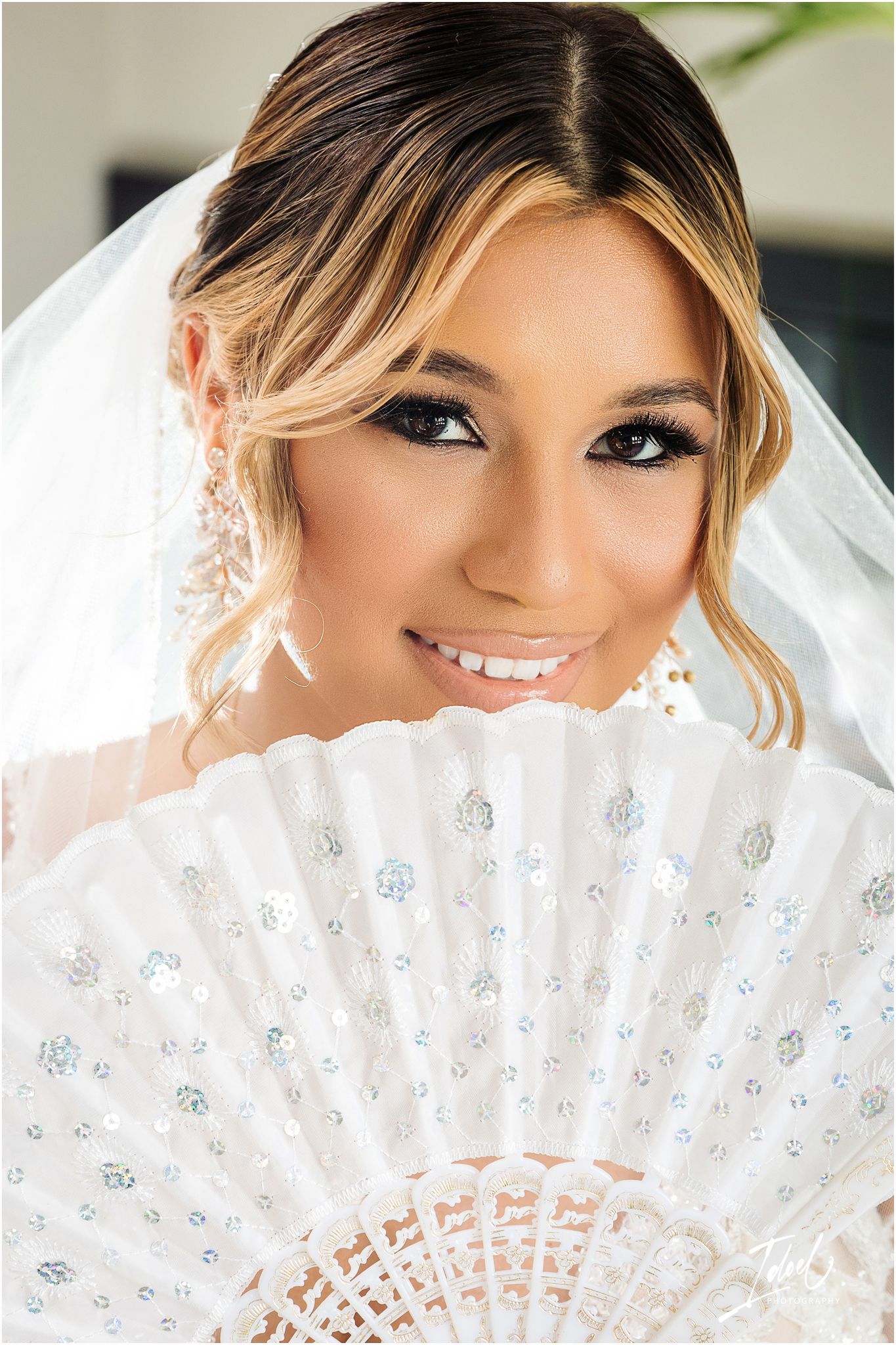 Close-up bridal portrait with white lace fan, veil, and glamorous makeup.