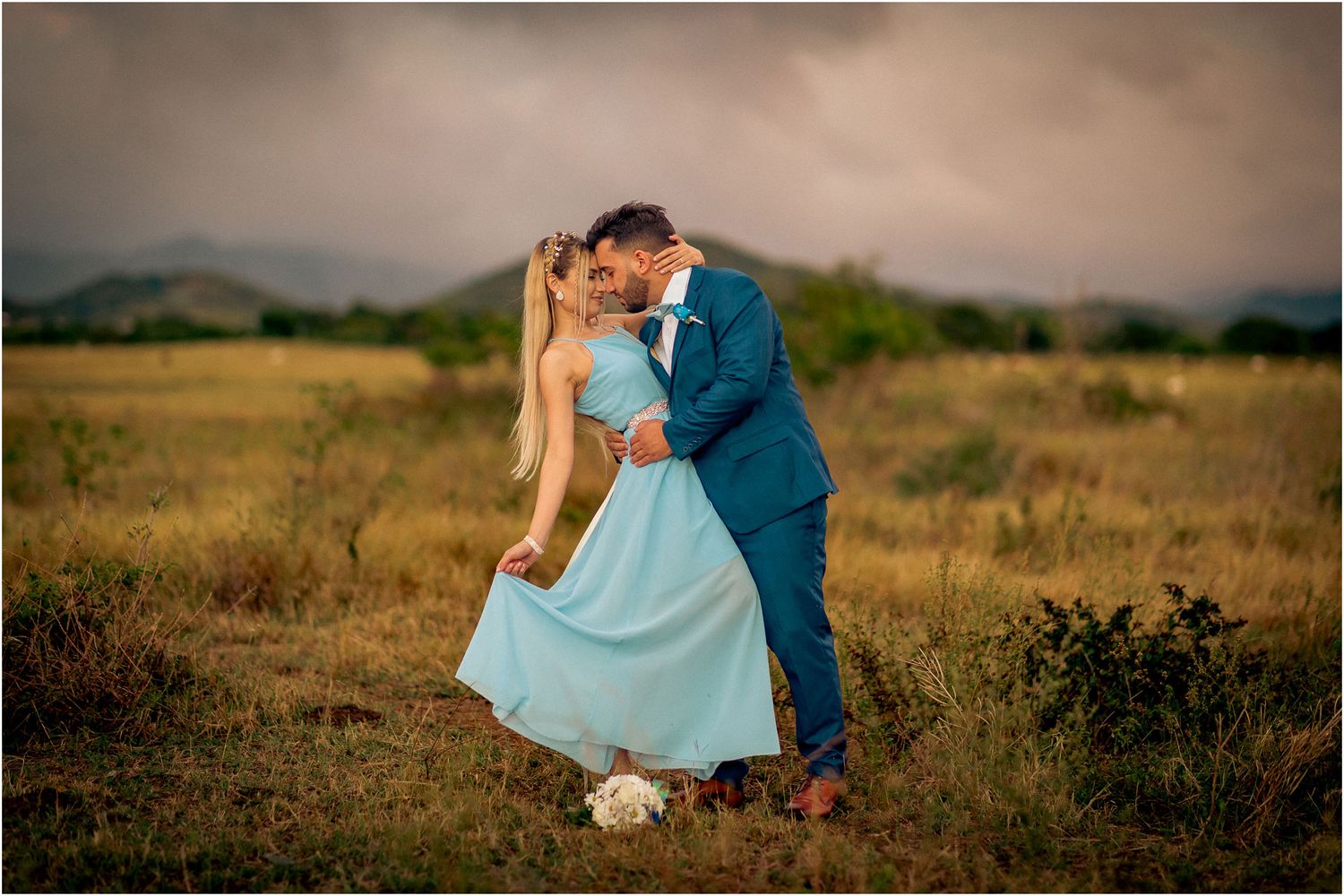 A romantic moment captured in a rustic field with moody storm clouds in the background.
