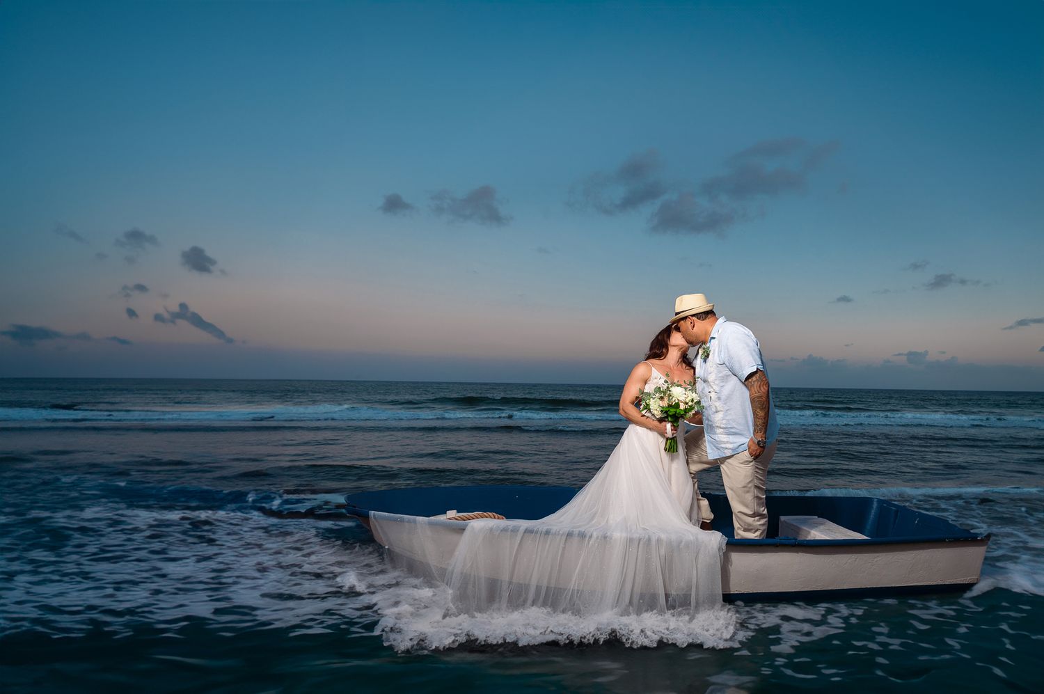 Bride and groom pose on beach at sunset with ocean waves in background.