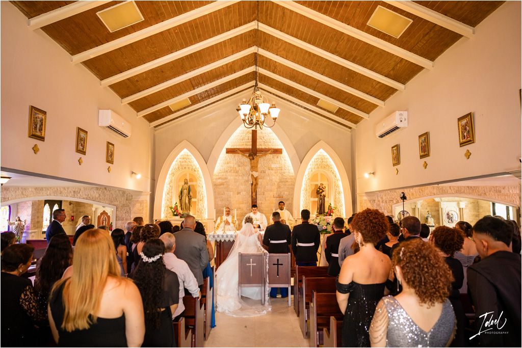 Interior of a traditional church during a wedding ceremony with guests seated under exposed wooden beams and arched altars.