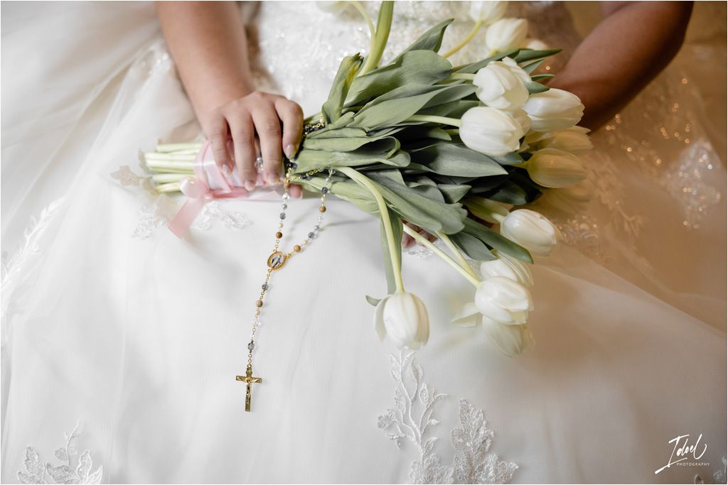 White tulip bouquet with rosary held against lace wedding dress.