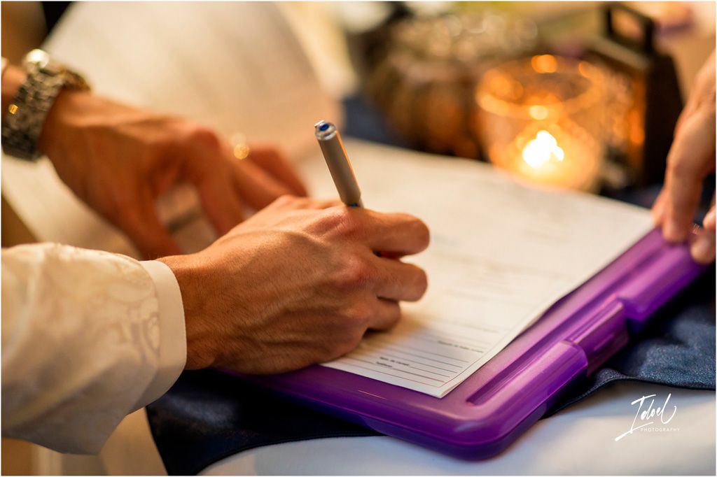 Hand holding a pen writing on paper next to a purple folder and glowing candle in soft lighting.